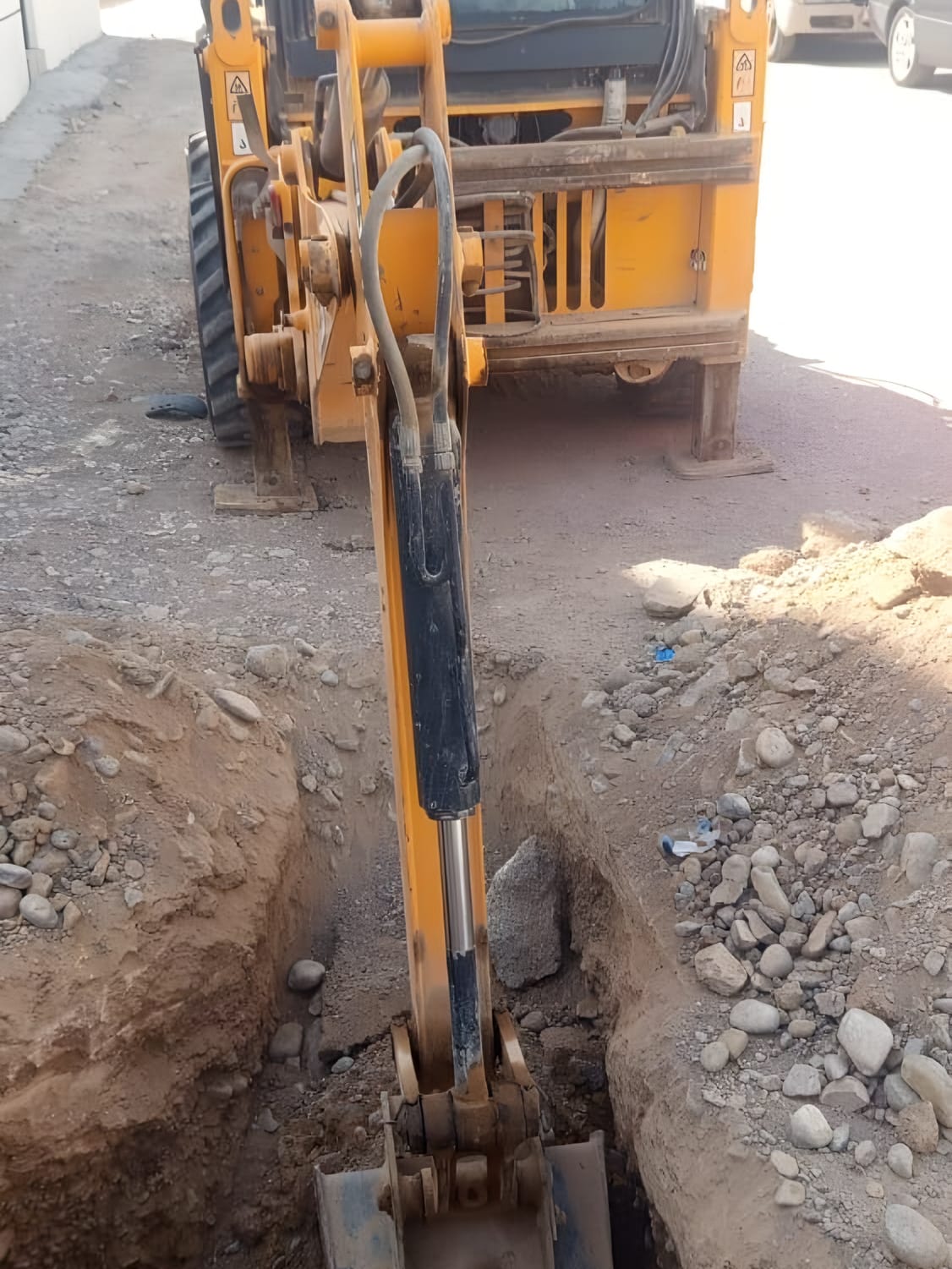 Backhoe cutting a service trench in a residential street