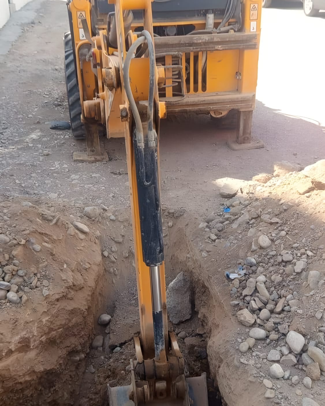 Backhoe cutting a service trench in a residential street