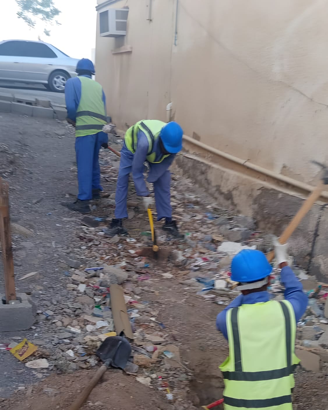 Hand excavation along a wall, the crew in hard hats and high-visibility vests