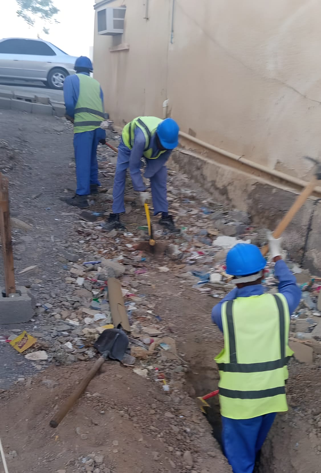 Hand excavation along a wall, the crew in hard hats and high-visibility vests