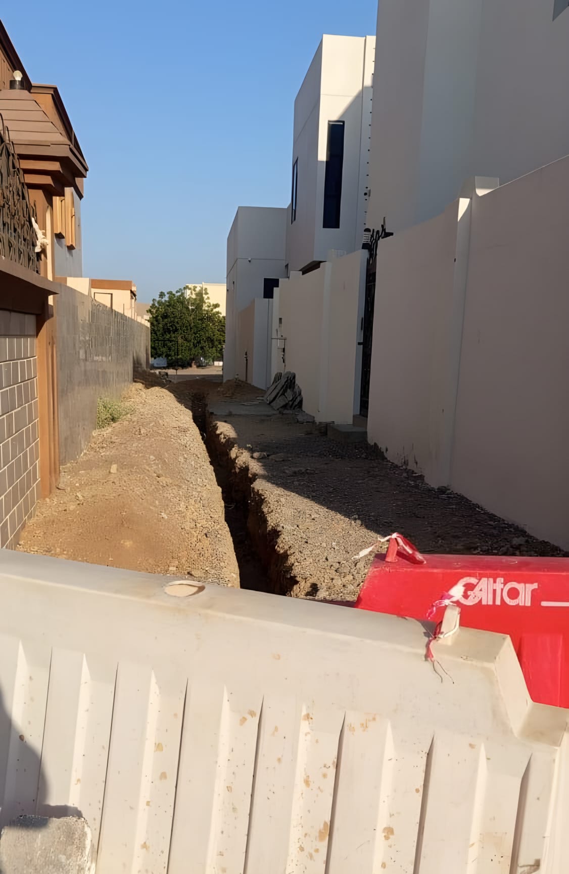 Open trench along a residential lane, barriers in place