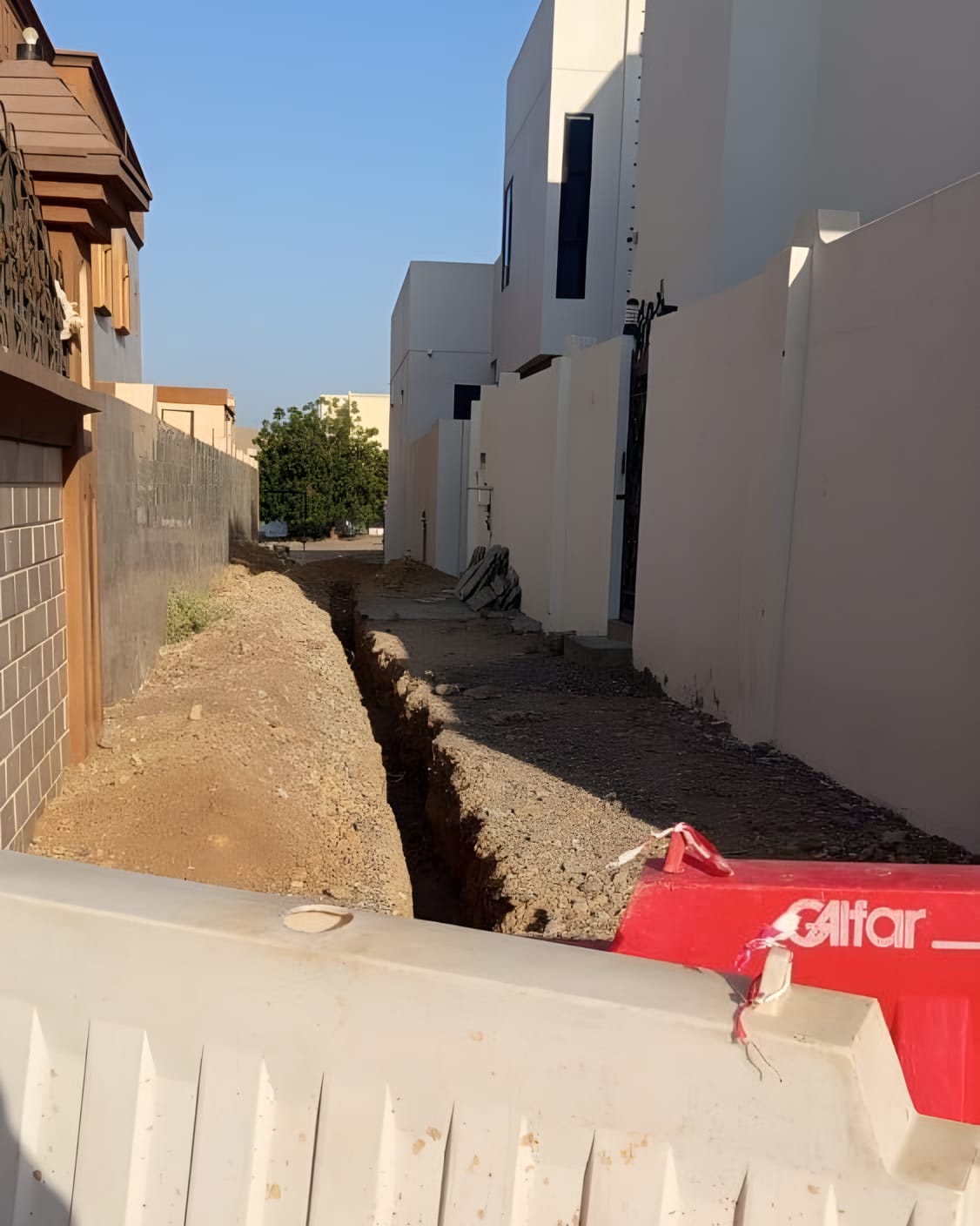 Open trench along a residential lane, barriers in place